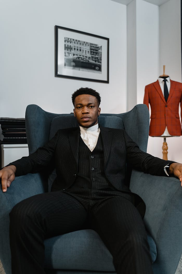 Elegant businessman in a black suit sitting confidently in a modern interior, exuding sophistication and style.